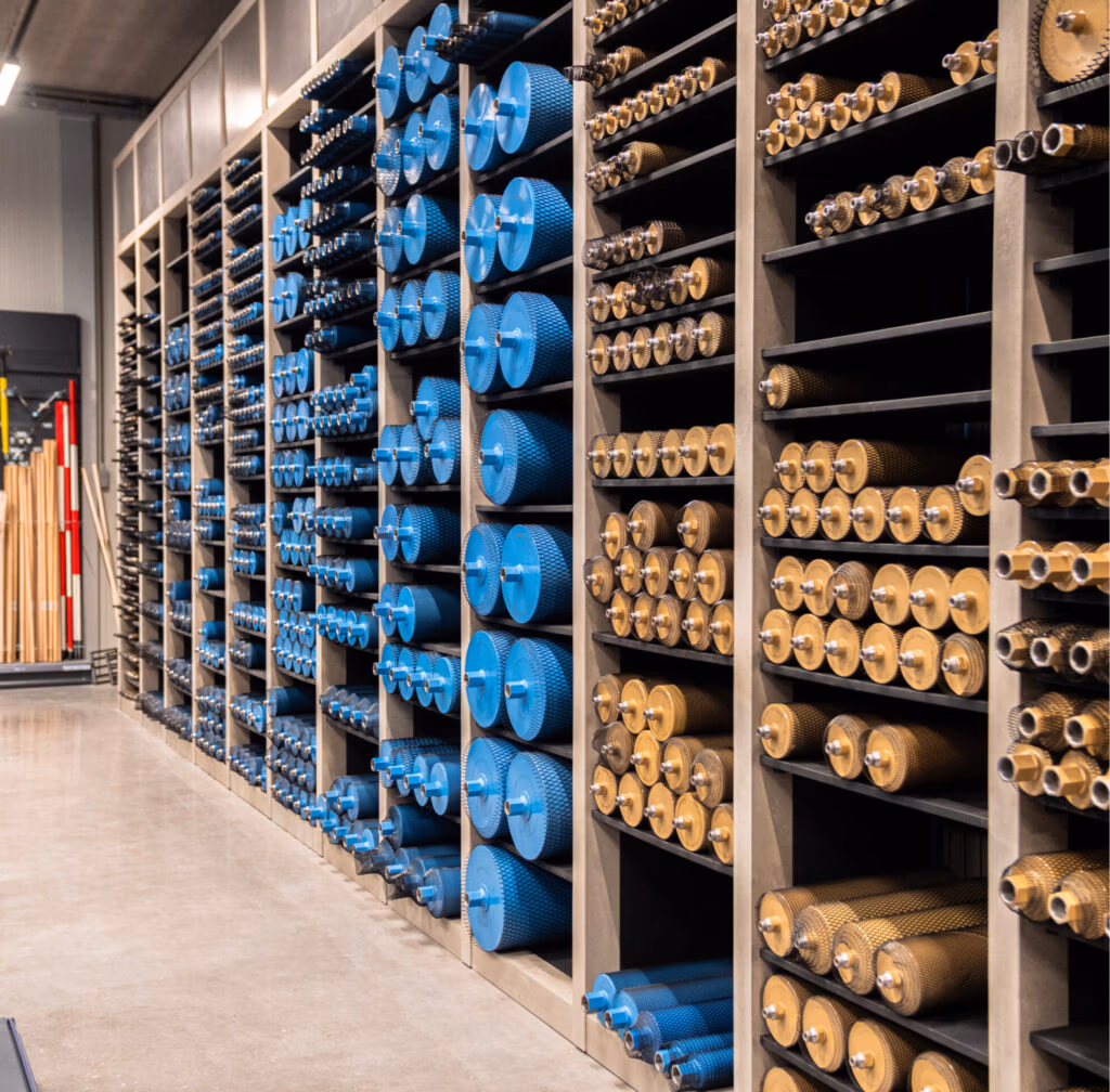 Planken vol met industriële rollen, cilinders en gereedschap zoals zaagbladen en diamantboren, voornamelijk in blauw en metaalglans, netjes gerangschikt in een magazijn met een gepolijste betonnen vloer.