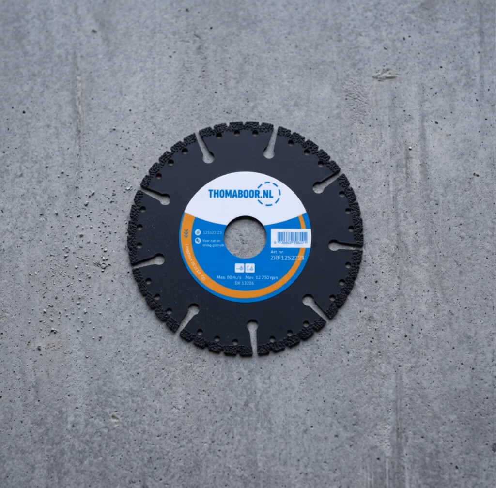 Een rond zwart zaagblad, dat deel uitmaakt van het assortiment kwaliteitszaagbladen, is in het midden voorzien van een blauw-wit Thomaboor-label en ligt plat op een grijs betonnen oppervlak.