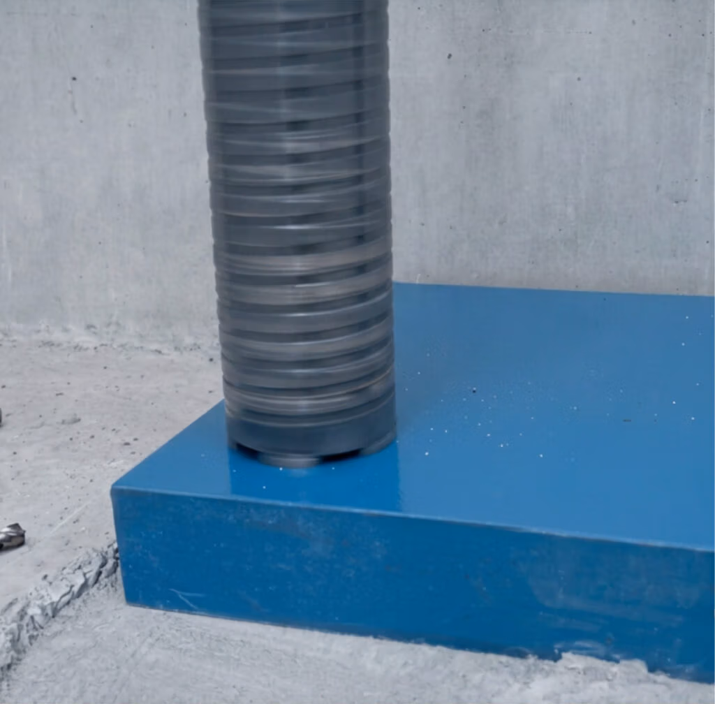 Een stapel doorzichtige plastic schijven, die op zaagbladen lijken, wordt door een machine op een blauw platform tegen een betonnen achtergrond samengedrukt.